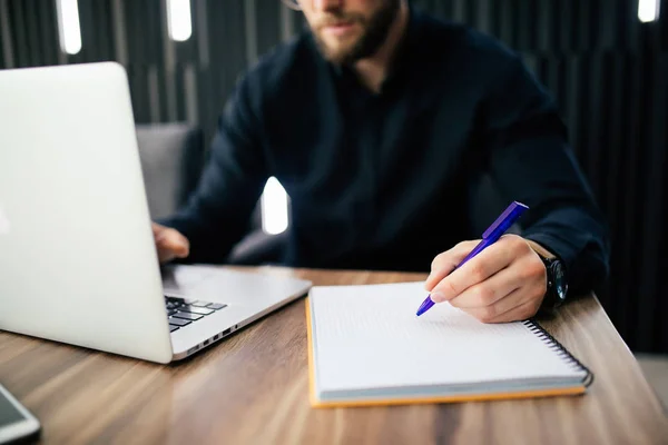 Hombre de negocios está escribiendo algo en el cuaderno de papel y computadora portátil en la mesa de madera, concepto de negocio . — Foto de Stock