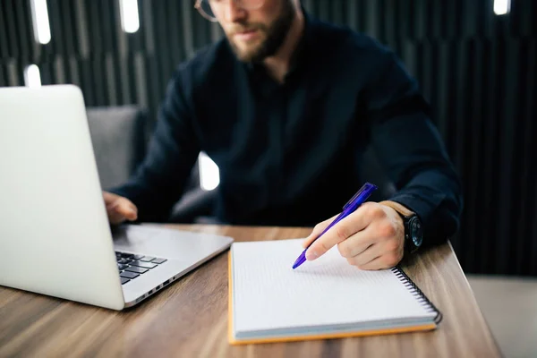 Hombre de negocios está escribiendo algo en el cuaderno de papel y computadora portátil en la mesa de madera, concepto de negocio . — Foto de Stock