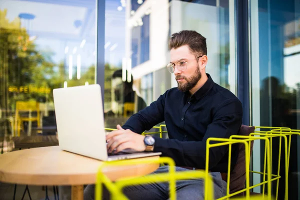 Hombre de negocios guapo utilizando el ordenador portátil moderno al aire libre, gerente exitoso que trabaja en la cafetería durante el descanso y la búsqueda de información en Internet en su computadora portátil — Foto de Stock