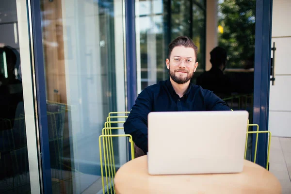 Ler skäggiga affärsman på telefonen arbetar på bärbar dator utanför caféet — Stockfoto