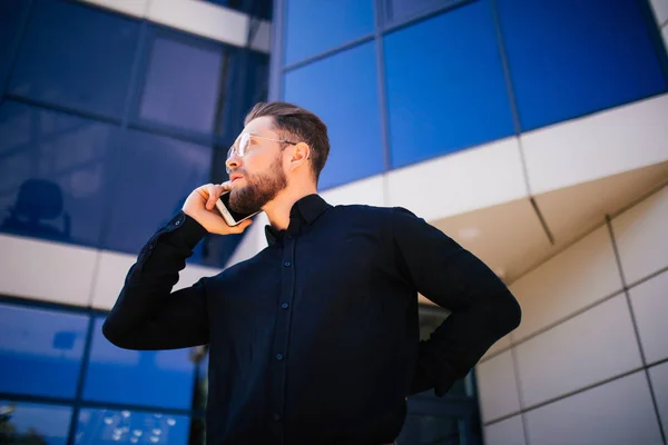 Portrét pohledný vousatých podnikatel mluvící telefon stojící poblíž kanceláře — Stock fotografie