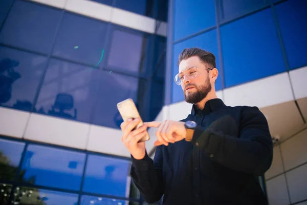 Lyckligt leende affärsman med moderna smartphone nära kontor, framgångsrik arbetsgivare att göra en deal när du står nära skyskrapa kontor — Stockfoto