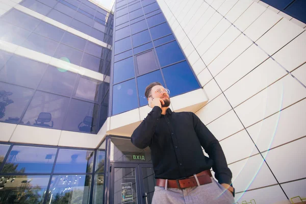 Confident man managing director is calling with mobile phone, while is standing in modern skyscraper interior.