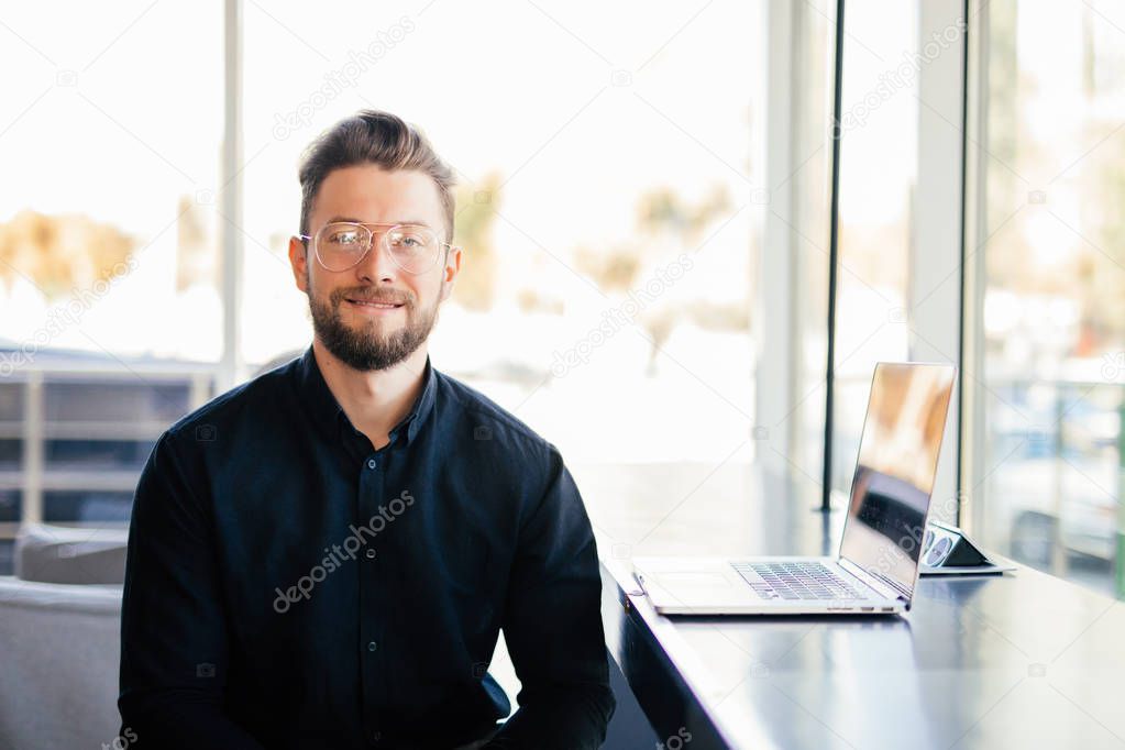 Portrait of young bearded business man in front of his working place in modern office