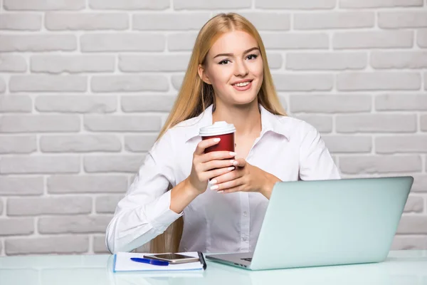 Joven hermosa mujer sosteniendo la taza de café mientras está sentada en su lugar de trabajo — Foto de Stock