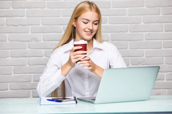 Joven hermosa mujer sosteniendo la taza de café mientras está sentada en su lugar de trabajo — Foto de Stock