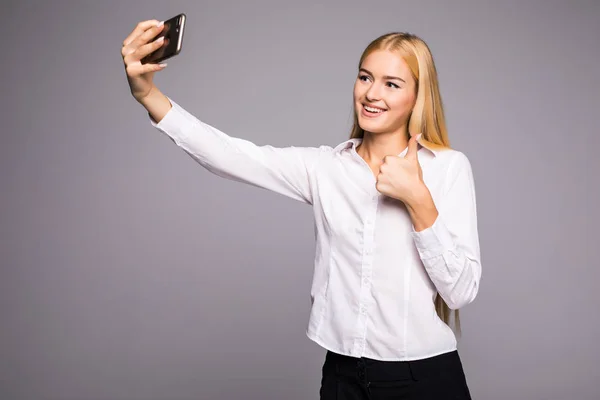 Улыбающаяся деловая женщина делает селфи фото на смартфоне. Стоя на сером фоне — стоковое фото