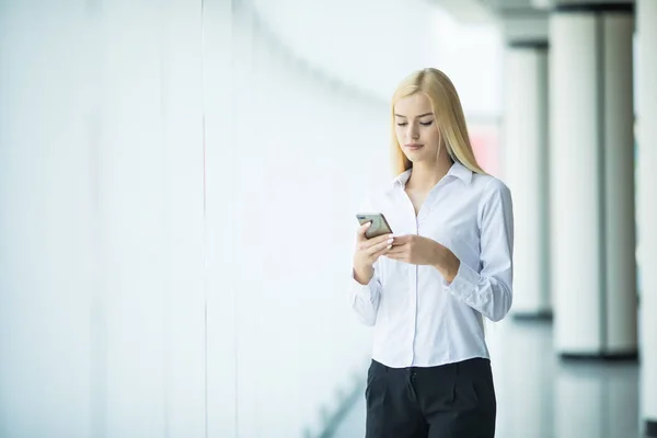 Üzleti nő használata vagy gépelés-ra telefon nagy office ablak modern, intelligens tér közelében. — Stock Fotó