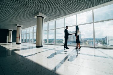 İş adamı ve iş kadını ofis önünde şehre bakan pencereler inşa ederken el sıkışıyor.