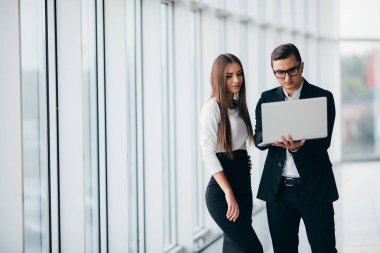 İş kadını ve işadamı duran ve boş ofis iç windows şehir manzaralı projede tartışırken laptop.