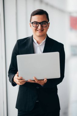 Genç gülümseyen işadamı dizüstü şirket konumunda kapalı temiz panoramik penceresini kullanma