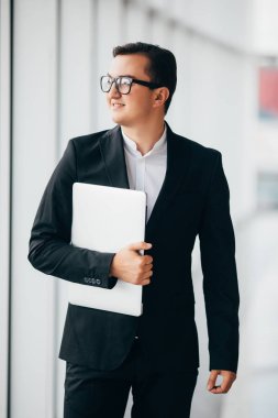 Ofiste bekleyen bir dizüstü bilgisayar üzerinde çalışan genç iş adamı. Bina cityscape bakan highrise ofis pencere Laptop ayakta tutan adam.