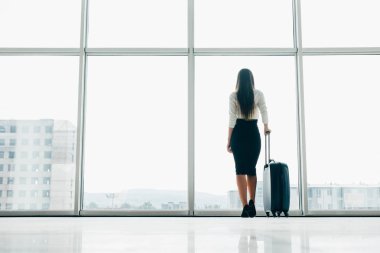 Gezgin işkadını bekleyen Havaalanı pencerede asfalt izlerken Bagaj ile Havaalanı lounge ayakta, uçuş gecikmeli. Kadın önce hareket yatılı kapısında.