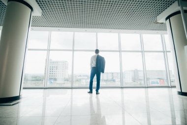 Genç işadamı ceket ile modern ofis panoramik pencerelere omuz üzerinden rahat