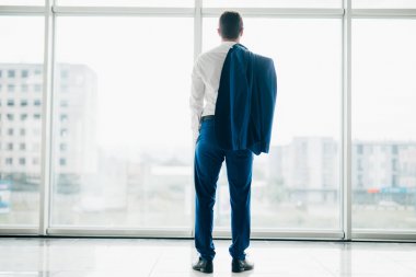 Genç işadamı ceket ile modern ofis panoramik pencerelere omuz üzerinden rahat