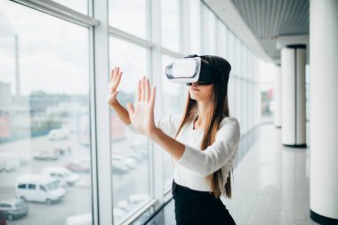 Parlak pencere dışında gökdelen manzaralı yakınındaki sanal gerçeklik gözlük kullanan güzel kız. İş kadını VR gözlük takıyor