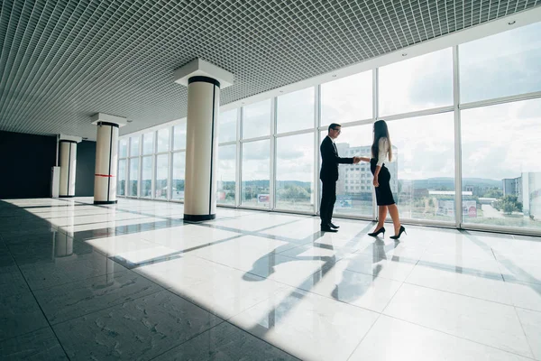 Homme d'affaires et femme serrant la main avec un sourire sur le fond des grandes fenêtres panoramiques dans un centre d'affaires moderne . — Photo