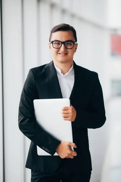 Joven hombre de negocios sonriente utilizando el ordenador portátil en la ubicación corporativa, interior limpio ventana panorámica — Foto de Stock