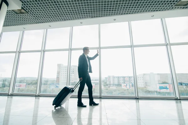 Der Geschäftsmann spaziert mit einem Koffer in der Nähe von Panoramafenstern im Flughafen — Stockfoto