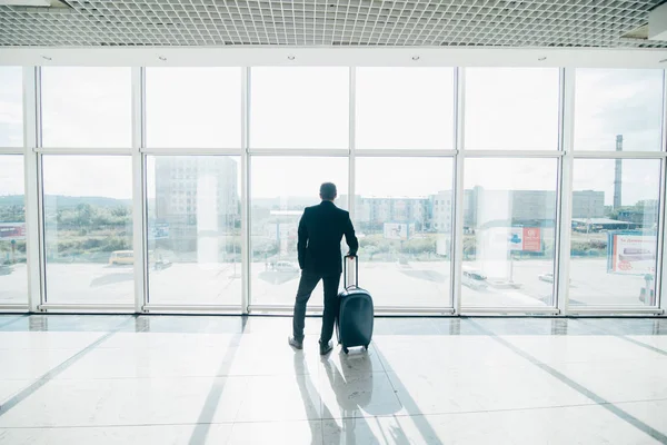 Dla podróżujących biznesmen w poczekalni czeka na lot i stojąc z wózek na bagaż. — Zdjęcie stockowe