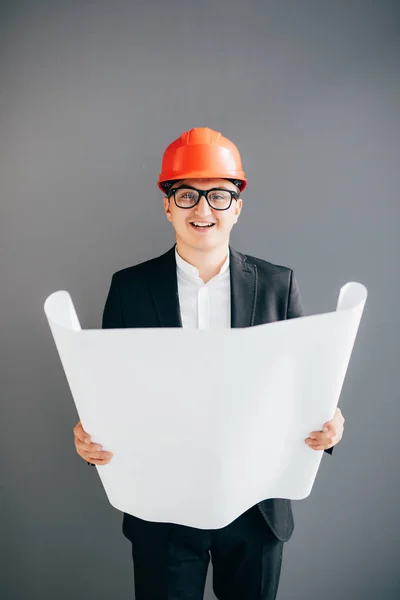 Portrait of Handsome young architect in protective helmet is studying draft, on gray background — Stock Photo, Image