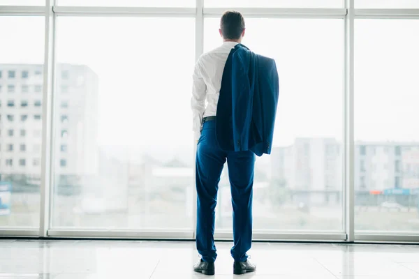 Молодой расслабленный бизнесмен с курткой за плечами в современных офисных панорамных окнах — стоковое фото