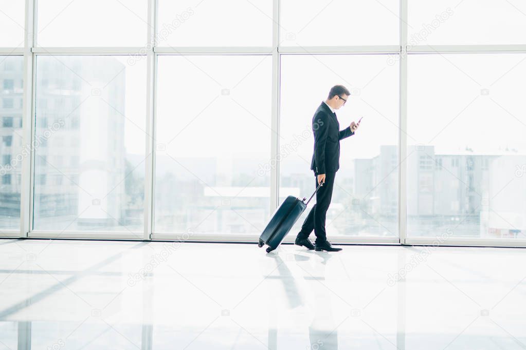 Businessman at international airport moving to terminal gate for airplane travel trip looking in phone in hand