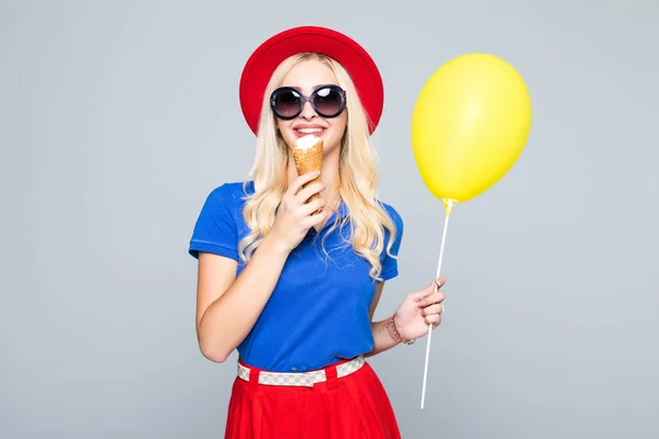 Divat, boldog, mosolygós nő sárga hőlégballon és fagylalt kúp visel szalma kalap és színes ruha felső szürke háttér — Stock Fotó