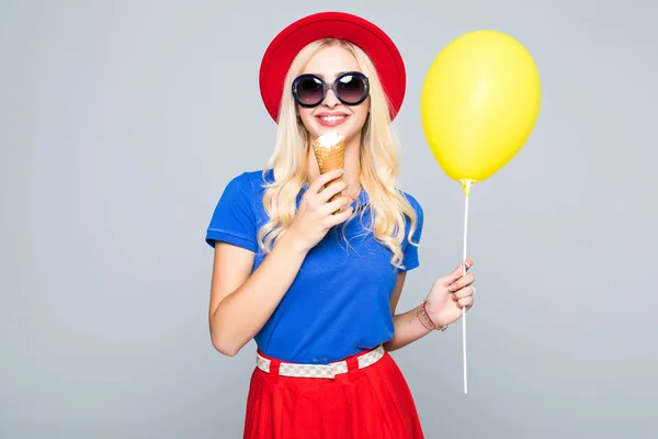 Divat, boldog, mosolygós nő sárga hőlégballon és fagylalt kúp visel szalma kalap és színes ruha felső szürke háttér — Stock Fotó