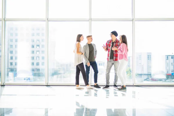 Vier Freunde unterhalten sich in heller Halle mit Panoramafenstern — Stockfoto