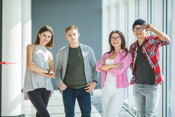 Ayakta ve kapalı gülümseyerek dört arkadaş. Ayak öğrenciler üniversitede.