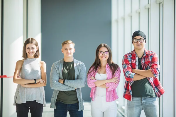 Quatro amigos de pé com as mãos cruzadas e sorrindo dentro de casa. Quatro estudantes na universidade . — Fotografia de Stock