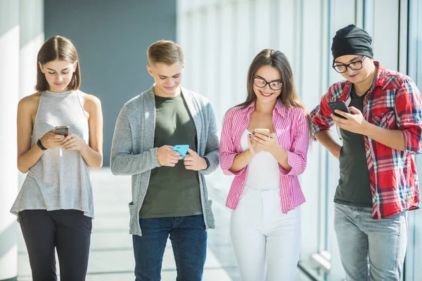 Fyra vänner som arbetar i företaget är beroende av från prylar, använder smarta telefoner och tablet för sökning sociala nätverk och meddelanden med vänner online — Stockfoto