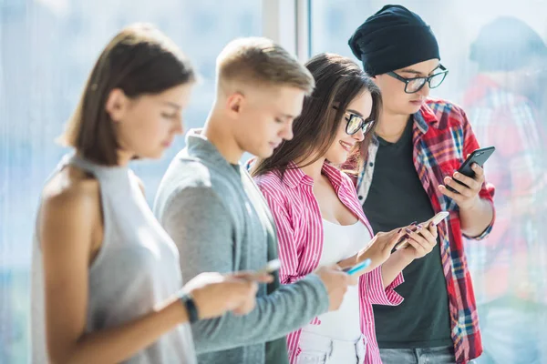 Cuatro amigos que trabajan en compañía siendo adictos desde gadgets, utilizando teléfonos inteligentes y tabletas para buscar en las redes sociales y mensajería con amigos en línea —  Fotos de Stock