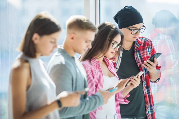 Groep jonge vrienden kijken naar hun smartphones zonder interactie elkaar binnenshuis. Concepten van levensstijl, technologieën en smartphone verslaving — Stockfoto