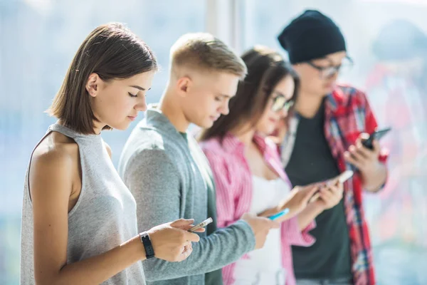 Groep jonge vrienden kijken naar hun smartphones zonder interactie elkaar binnenshuis. Concepten van levensstijl, technologieën en smartphone verslaving — Stockfoto