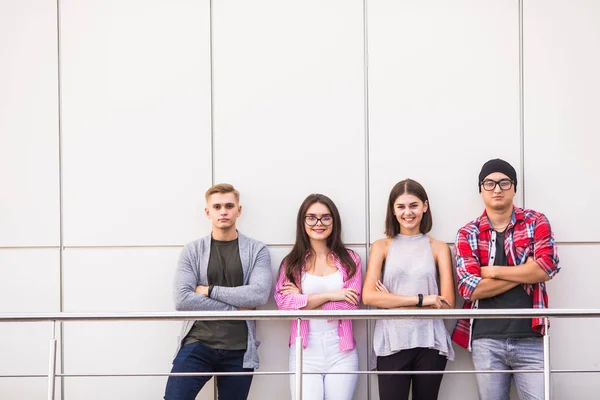 Grupa czterech młodych uśmiechający się ludzie sobie Stylowa odzież na co dzień patrząc na kamery stojący w biurze światła lub Uniwersytetu. — Zdjęcie stockowe