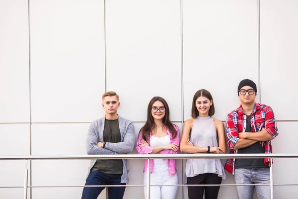 Group of four young smiling people wearing stylish casual clothing looking at camera standing in light office or university.