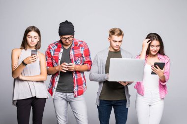 Gençlerin grup kanepede oturan ve dijital tablet ve beyaz arka plan üzerinde izole dizüstü kullanarak mutlu.