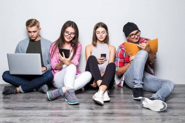 Yere oturmak ve çalışmak için modern teknolojiyi kullanarak dostu gülümseyen öğrenci grubu