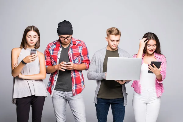 Gençlerin grup kanepede oturan ve dijital tablet ve beyaz arka plan üzerinde izole dizüstü kullanarak mutlu.