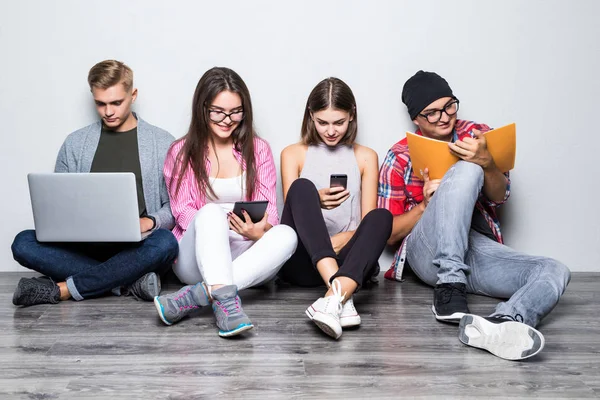 Grupo de simpáticos estudiantes sonrientes sentados en el suelo y utilizando la tecnología moderna para estudiar —  Fotos de Stock