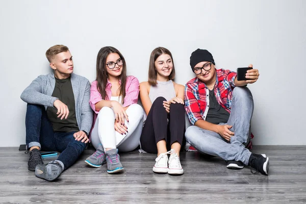 Ομάδα όμορφη μαθητών σε casual ρούχα κάνει selfie χρησιμοποιώντας ένα smartphone και χαμογελώντας, ενώ κάθονται μαζί στο πάτωμα — Φωτογραφία Αρχείου