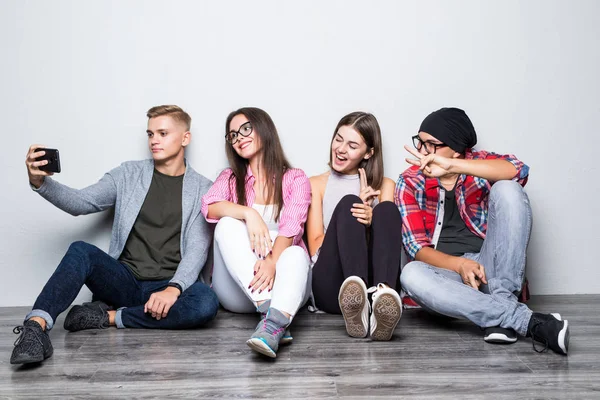 Grupp vackra studenter i casual kläder gör selfie med en smartphone och ler medan sitter ihop på golvet — Stockfoto