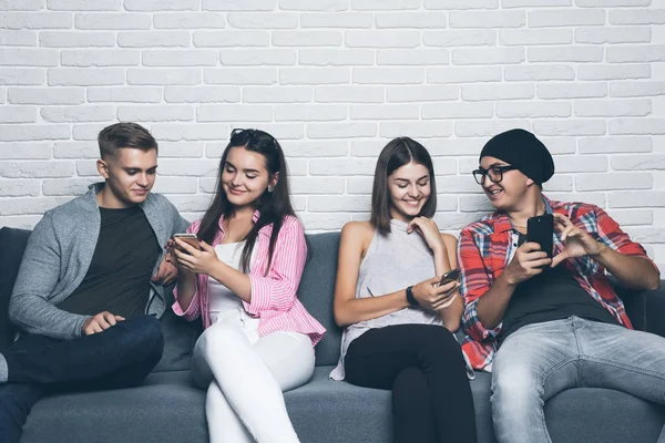 Jovens amigos a olhar para o telemóvel. Sentados no sofá e ignorando uns aos outros com os telefones inteligentes . — Fotografia de Stock