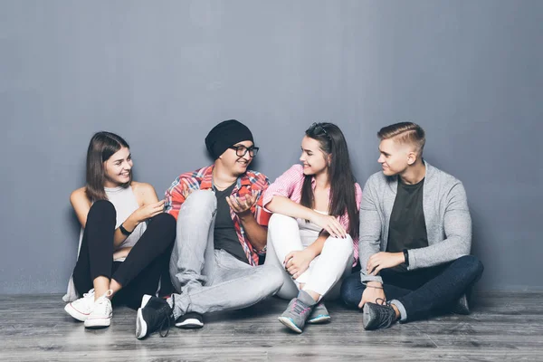 Grupo de estudantes bonitos em roupas casuais usando gadgets, conversando e sorrindo enquanto sentados juntos no chão — Fotografia de Stock