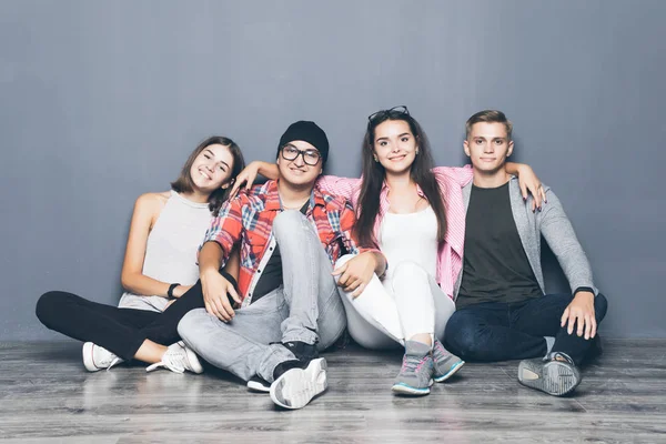 Güzel genç arkadaşlar sarılma, kameraya bakıyor ve gri arka plan üzerinde katta otururken gülümseyen