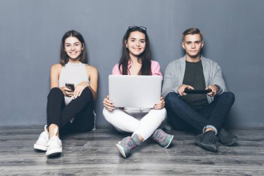 Üç genç arkadaş oturma odasında yerde aygıtları kullan