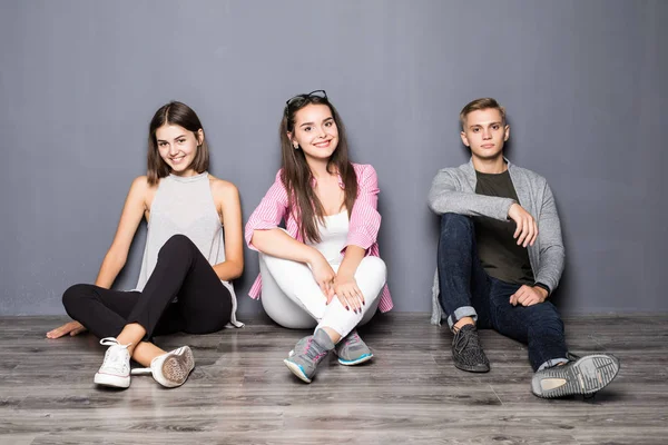 Gruppo di amici seduti sul pavimento su sfondo grigio — Foto Stock