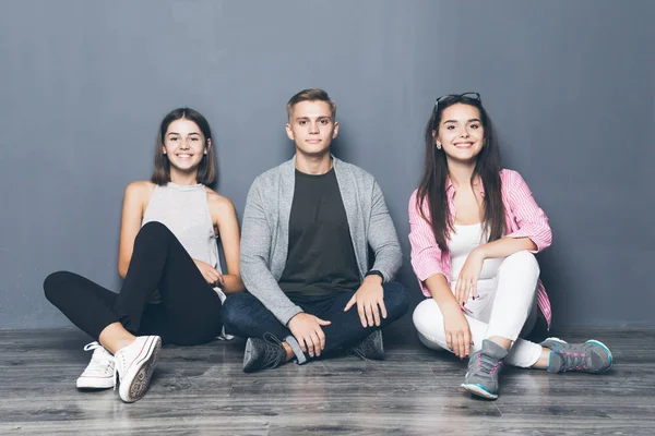 Grupo de amigos sentados no chão em fundo cinza — Fotografia de Stock